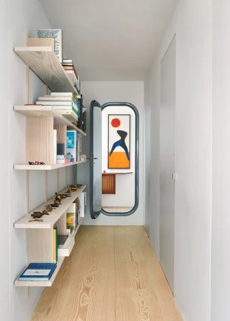 Hallway featuring a blonde wood floor, white walls, and a built-in bookshelf. A door offers a glimpse into another room with artwork.