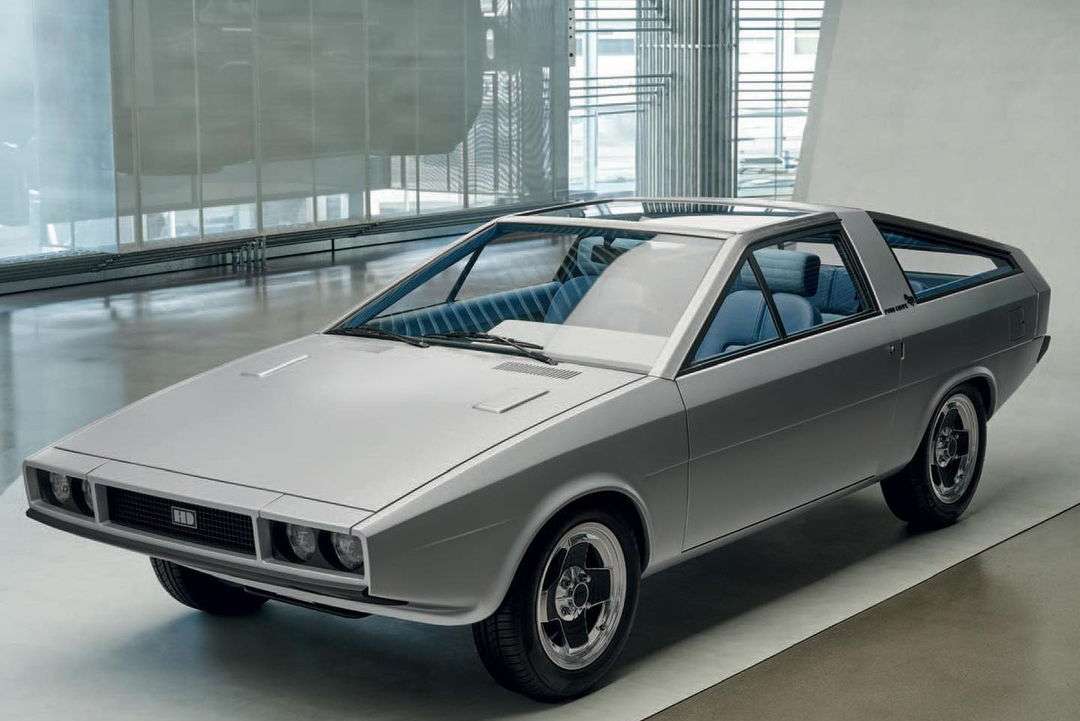 Silver Hyundai Pony Coupe concept car parked indoors with visible black tires, blue interior, and a white geometric background wall.