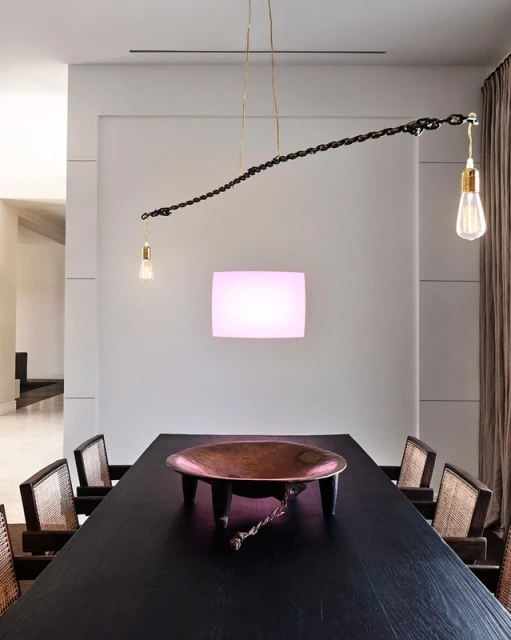 Dining room interior with a long, dark wood table, copper bowl centerpiece, and unique chain-link chandelier with exposed bulbs.