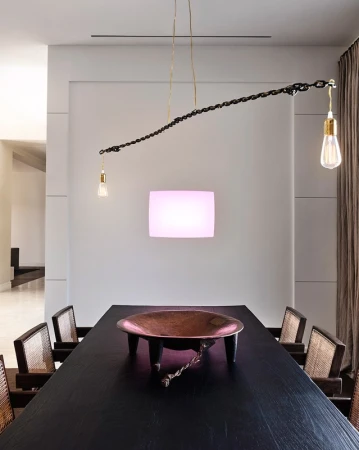 Dining room interior with a long, dark wood table, copper bowl centerpiece, and unique chain-link chandelier with exposed bulbs.