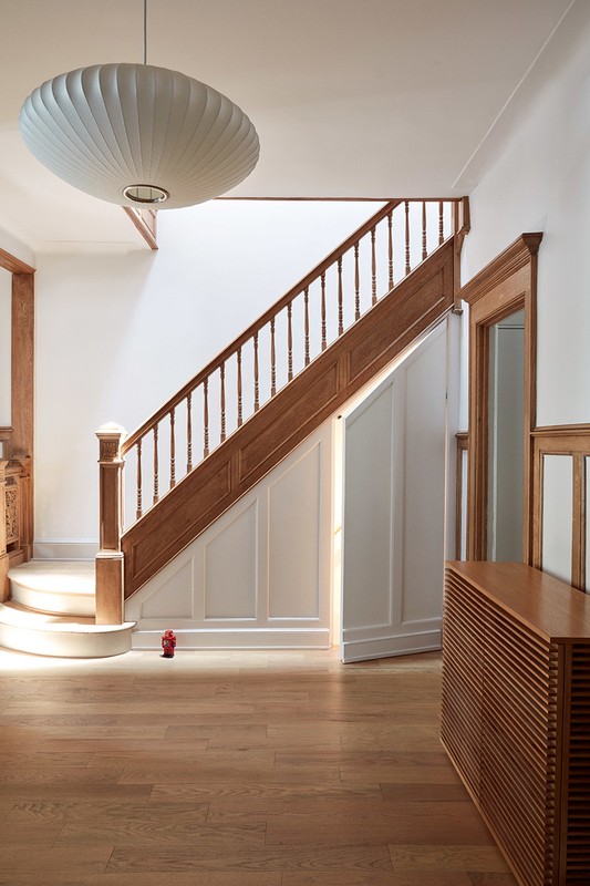 Interior view of a home hallway with wooden stairs leading upwards, a mid-century modern light fixture, and wooden floors and trim.