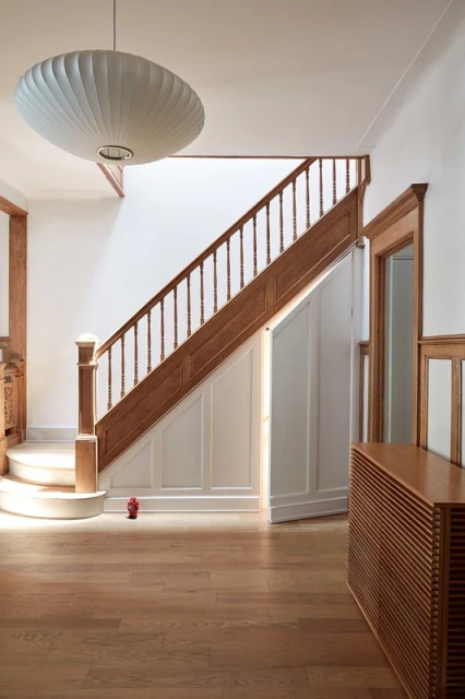 Interior view of a home hallway with wooden stairs leading upwards, a mid-century modern light fixture, and wooden floors and trim.