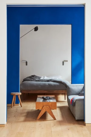 Interior view through a bold blue doorway framing a modern bedroom and a living room with wooden flooring.