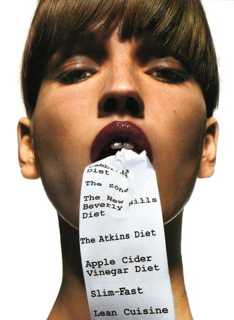 Adult female poses with a crumpled receipt listing various diets in her mouth in a studio shot with bright, even lighting on white.