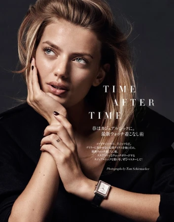 Close-up portrait of a woman resting her chin on her hand, wearing a dark jacket and a rectangular wristwatch against a dark grey background.