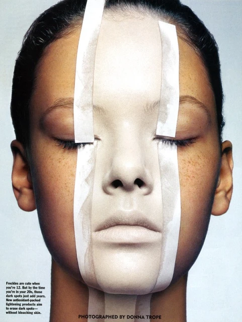 Close-up studio portrait of an adult woman with light brown skin and freckles, with white strips covering parts of her face.