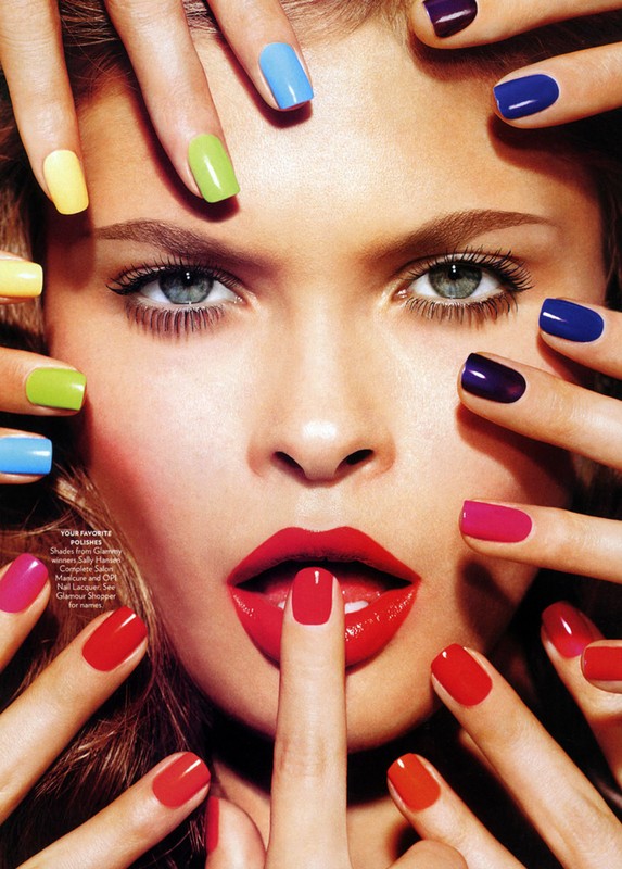 Close-up of a woman's face surrounded by hands with multicolored manicured nails, red lipstick, and a finger touching her lips.