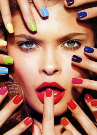 Close-up of a woman's face surrounded by hands with multicolored manicured nails, red lipstick, and a finger touching her lips.