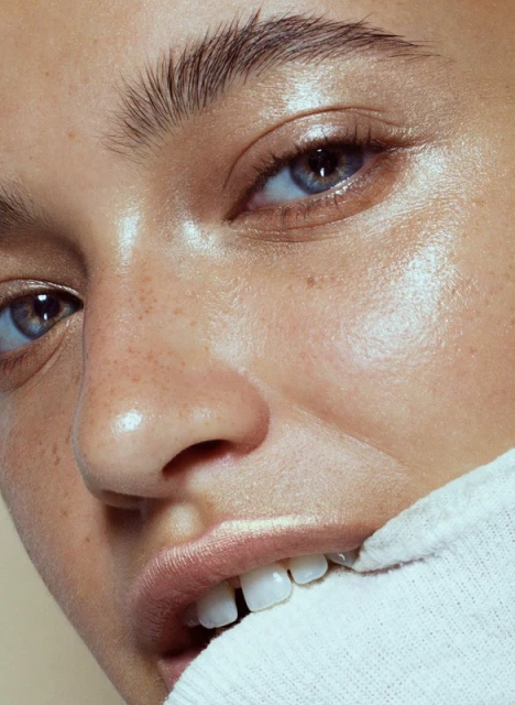 Close-up of a woman's face with light skin, blue eyes, and freckles, biting a white collar, emphasizing beauty and natural skin texture.