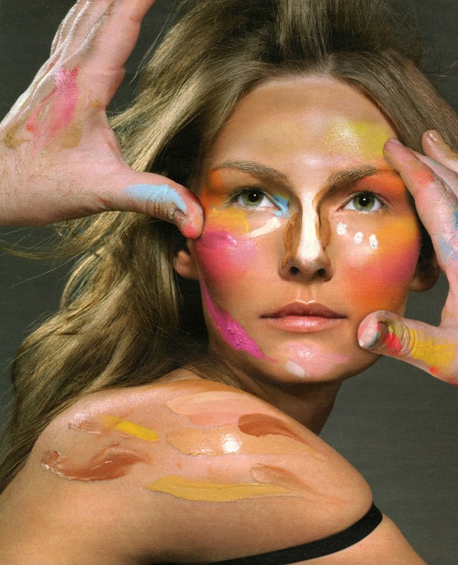 Model with artistic makeup application in varied colors, with hands applying additional makeup, beauty and fashion concept.