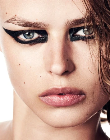 Close-up portrait of a woman with dramatic black winged eyeliner and freckles featuring make-up by Christopher Ardoff