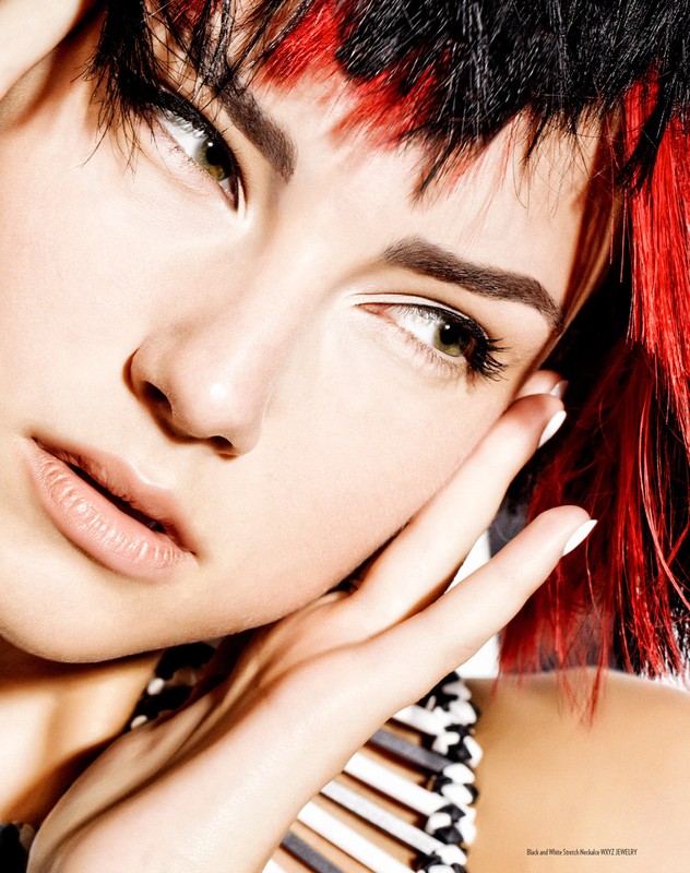 Close-up studio shot of a young adult female with black and red hair, light skin, light eyes, hands near her face, and wearing a black and white top.