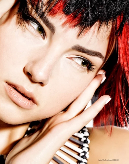 Close-up studio shot of a young adult female with black and red hair, light skin, light eyes, hands near her face, and wearing a black and white top.
