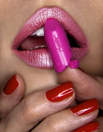 Close-up of shimmering metallic pink lips biting a bright magenta lipstick with fingers showing glossy red nail polish.