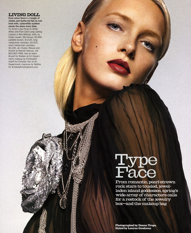 Fashion editorial shot of a blonde woman with pale skin, wearing a sheer black top and multiple silver necklaces and a sequined bag.