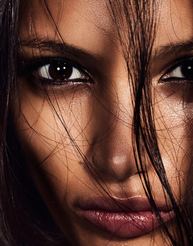 Close-up portrait of a young adult female with dark brown hair partially obscuring her face. She is looking at the camera.