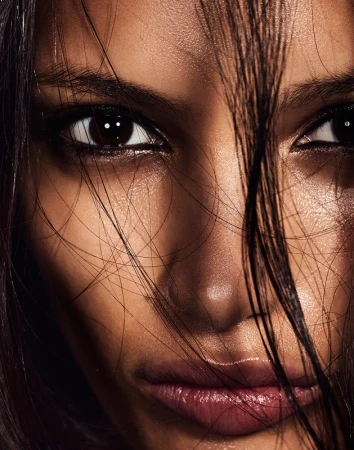 Close-up portrait of a woman with dark hair strands across her face, winged eyeliner, and glossy lips.