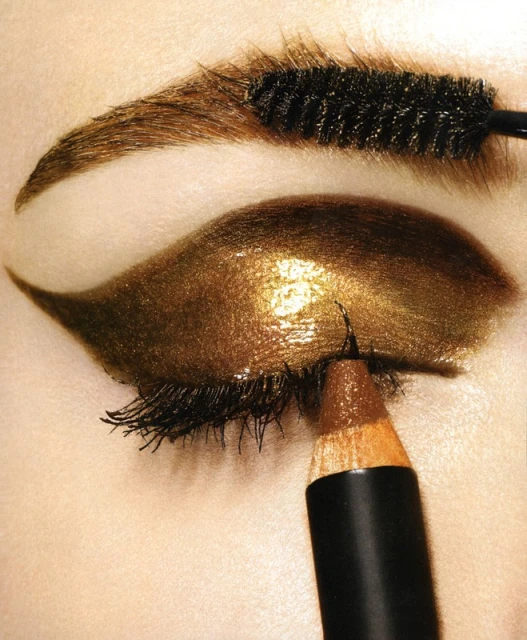 Close-up of a person's eye with bronze eyeshadow and eyeliner applied with a brush and pencil for a beauty editorial shot.