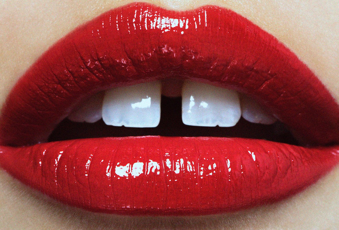 Close-up of red glossy lips with a small gap between the front teeth, showcasing beauty and dental features in a vibrant, detailed view.