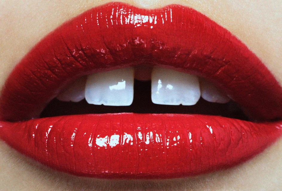 Close-up of red glossy lips with a small gap between the front teeth, showcasing beauty and dental features in a vibrant, detailed view.
