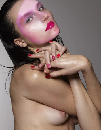 Glamorous studio shot of a partially nude adult woman with creative pink makeup and red nails against a grey backdrop, shoulder-up view.