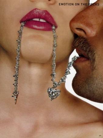 Close-up of a woman with vibrant pink lipstick holding a diamond necklace in her mouth while a man kisses her neck