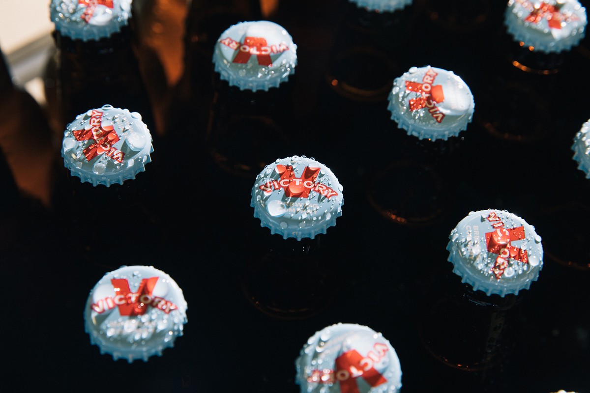Close-up of brown beer bottles with light blue caps, each displaying the word 'Victory' in red. Water droplets accent the caps.