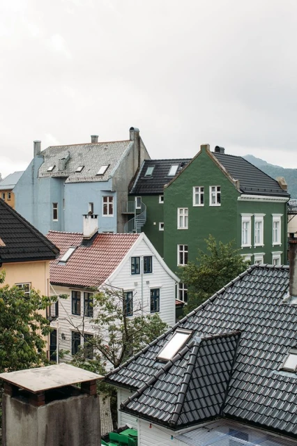 Residential neighborhood featuring a cluster of multi-story houses with various roof styles and colors against a cloudy sky.