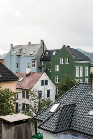 Residential neighborhood featuring a cluster of multi-story houses with various roof styles and colors against a cloudy sky.