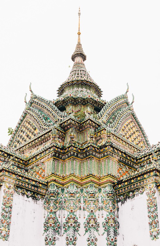 Elaborate architecture of a Thai temple's multi-tiered roof with intricate tiling, decorative spire, and detailed ornamentation against a bright sky.