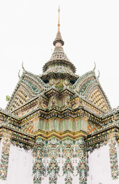 Elaborate architecture of a Thai temple's multi-tiered roof with intricate tiling, decorative spire, and detailed ornamentation against a bright sky.