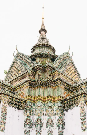 Elaborate architecture of a Thai temple's multi-tiered roof with intricate tiling, decorative spire, and detailed ornamentation against a bright sky.