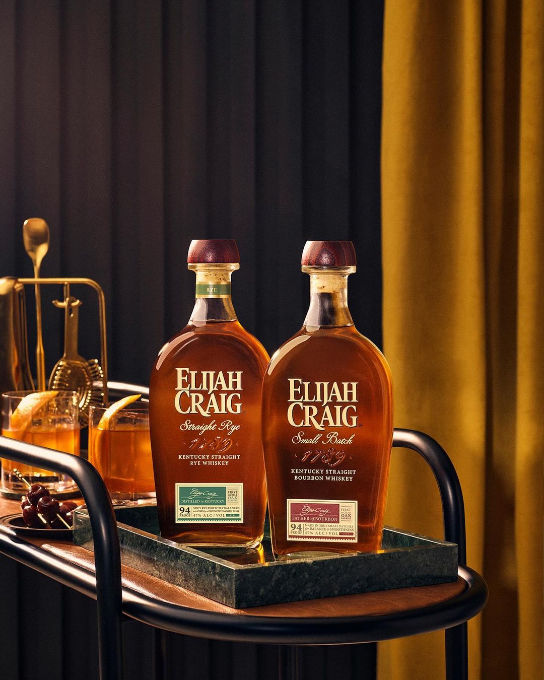 Two Elijah Craig bourbon bottles on a bar cart with cocktail; warm lighting, dark background, inviting ambiance, showcasing beverage appeal.
