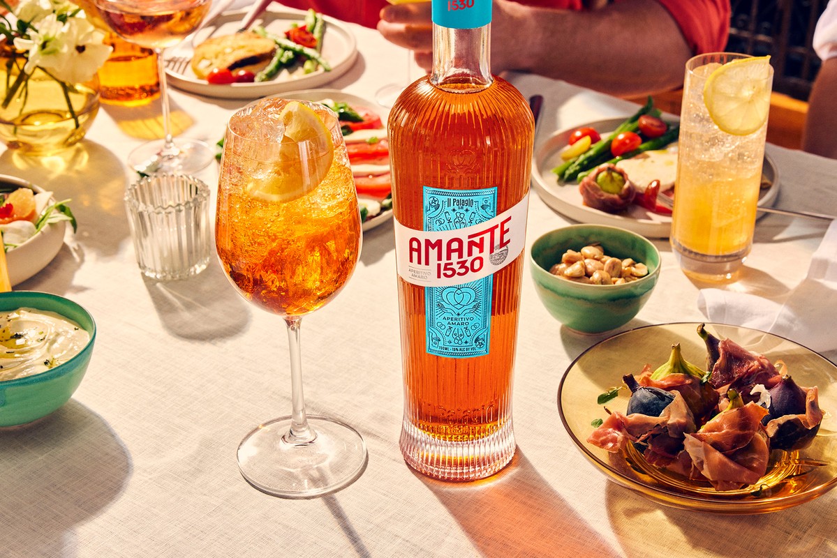 Amante 1530 aperitivo bottle and cocktail glass with lemon slice on table setting with drinks and plates of food at brunch.