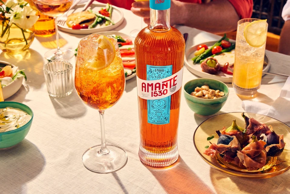 Amante 1530 aperitivo bottle and cocktail glass with lemon slice on table setting with drinks and plates of food at brunch.