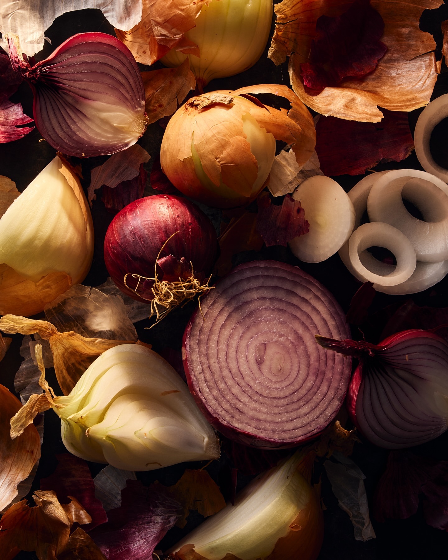 Overhead shot of vibrant red and yellow onions, some sliced, alongside scattered onion skins, creating a textural food still life.