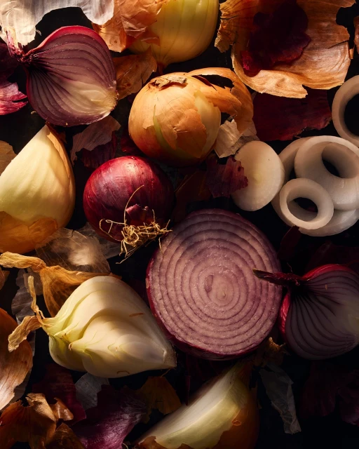 Overhead shot of vibrant red and yellow onions, some sliced, alongside scattered onion skins, creating a textural food still life.