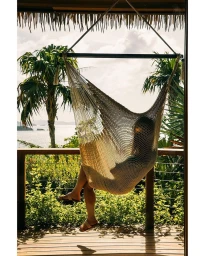 Person relaxing in a woven hammock on a tropical balcony overlooking palm trees and the ocean by Christopher Simpson