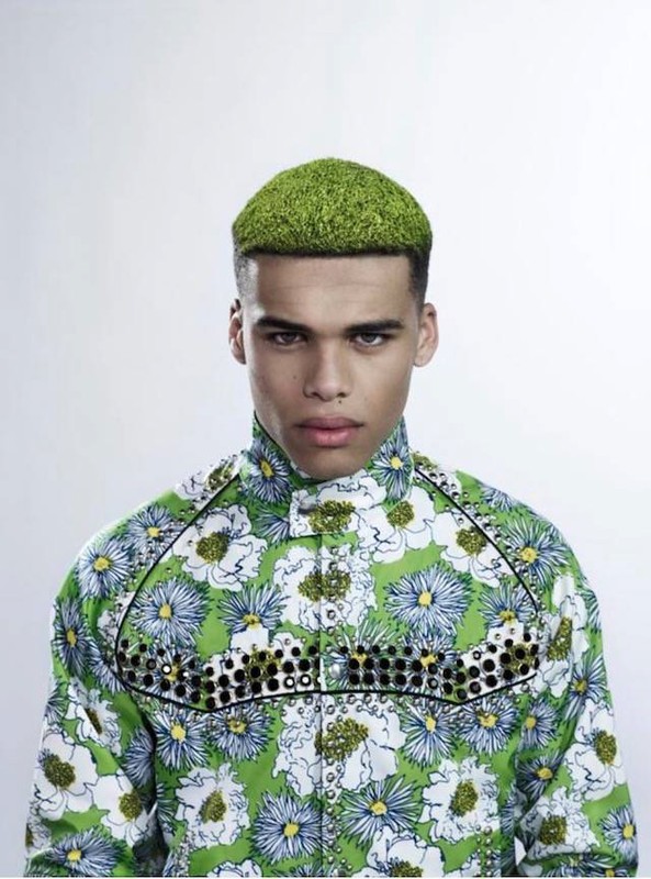 Portrait of a man with short green textured hair wearing a green floral print jacket against a white background.