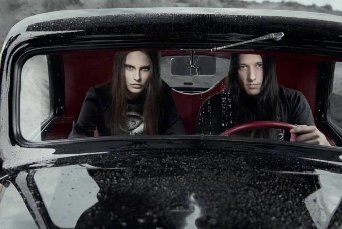 Two people in the front seats of a black vintage car, one driving and the other in the passenger seat, looking out.