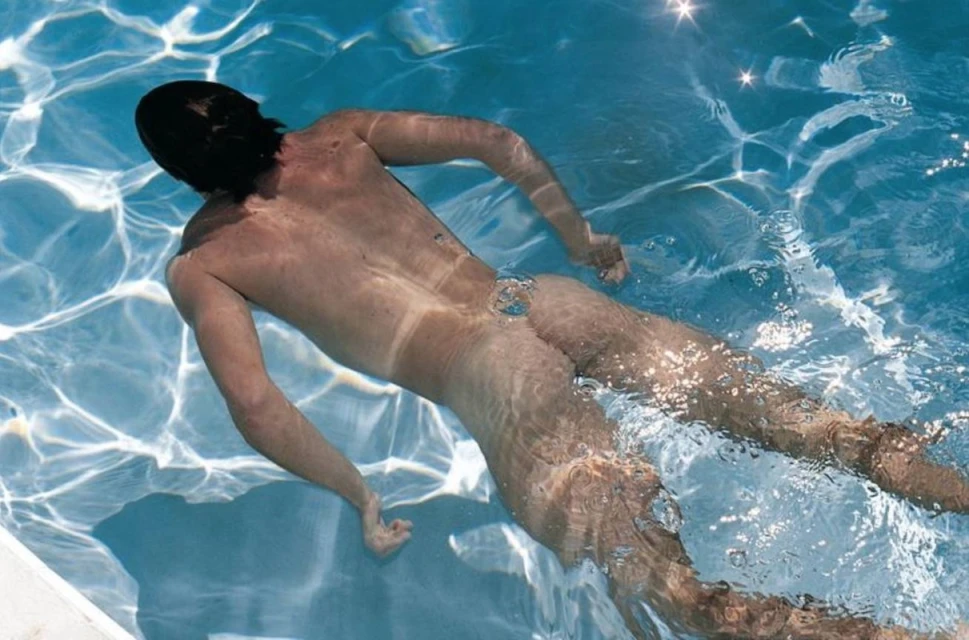 An adult is swimming underwater in a pool, showcasing the serene blue water reflecting sunlight, creating a peaceful underwater scene.