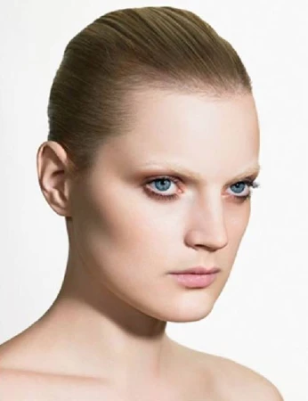 Close-up portrait of an adult woman with fair skin and blue eyes against a bright white backdrop, showcasing her face and hairstyle.