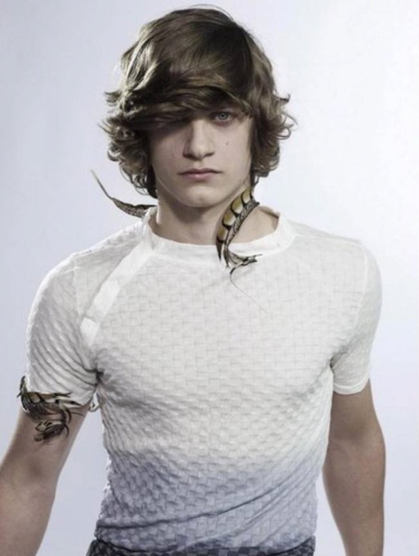 Young male model with layered brown hair wearing a white textured t-shirt against a plain white studio background.