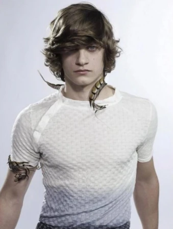 Young male model with layered brown hair wearing a white textured t-shirt against a plain white studio background.