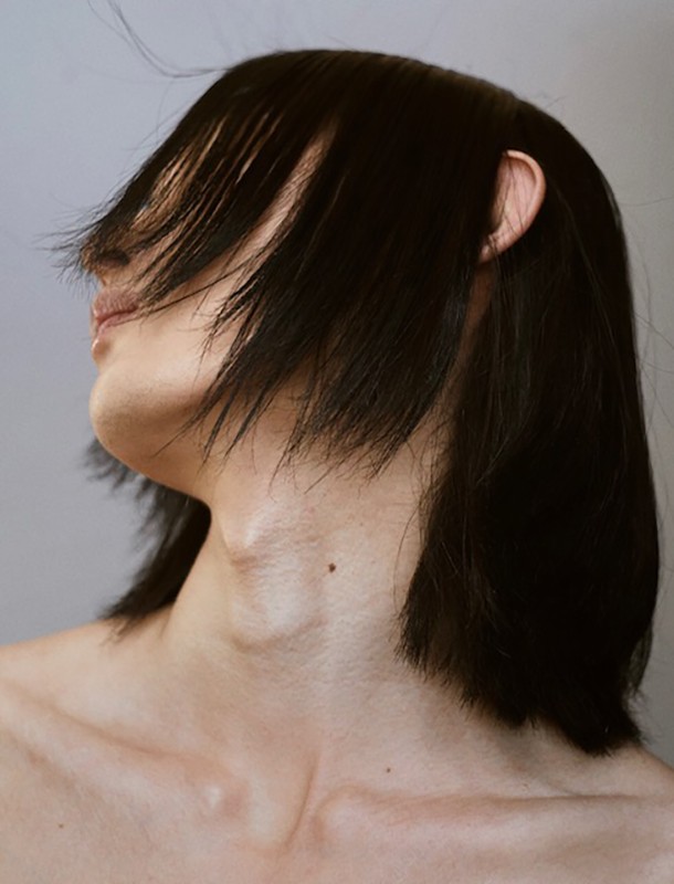 Close-up portrait of an adult woman with short, dark hair covering part of her face, shot in a photo studio with neutral lighting.