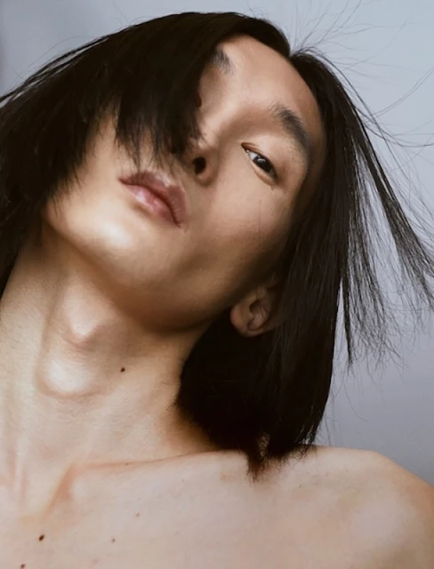Close-up studio portrait of an Asian male model with dark hair, posing in soft, diffused lighting with a neutral expression.