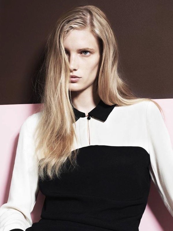 Blonde woman in a black and white top poses in front of pink and brown background in this medium studio portrait.