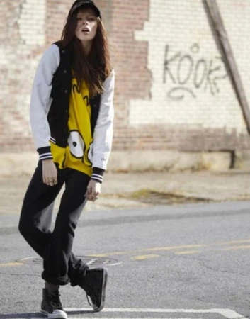Young woman in a black and white baseball jacket and yellow graphic t-shirt posing on an asphalt street in Los Angeles.