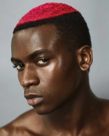 Close-up portrait of a Black man with short dark hair featuring a vibrant pink dyed stripe on top.