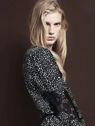 Portrait of a blonde woman wearing a black and white patterned dress against a dark brown background with hair styled by Colin Gold.